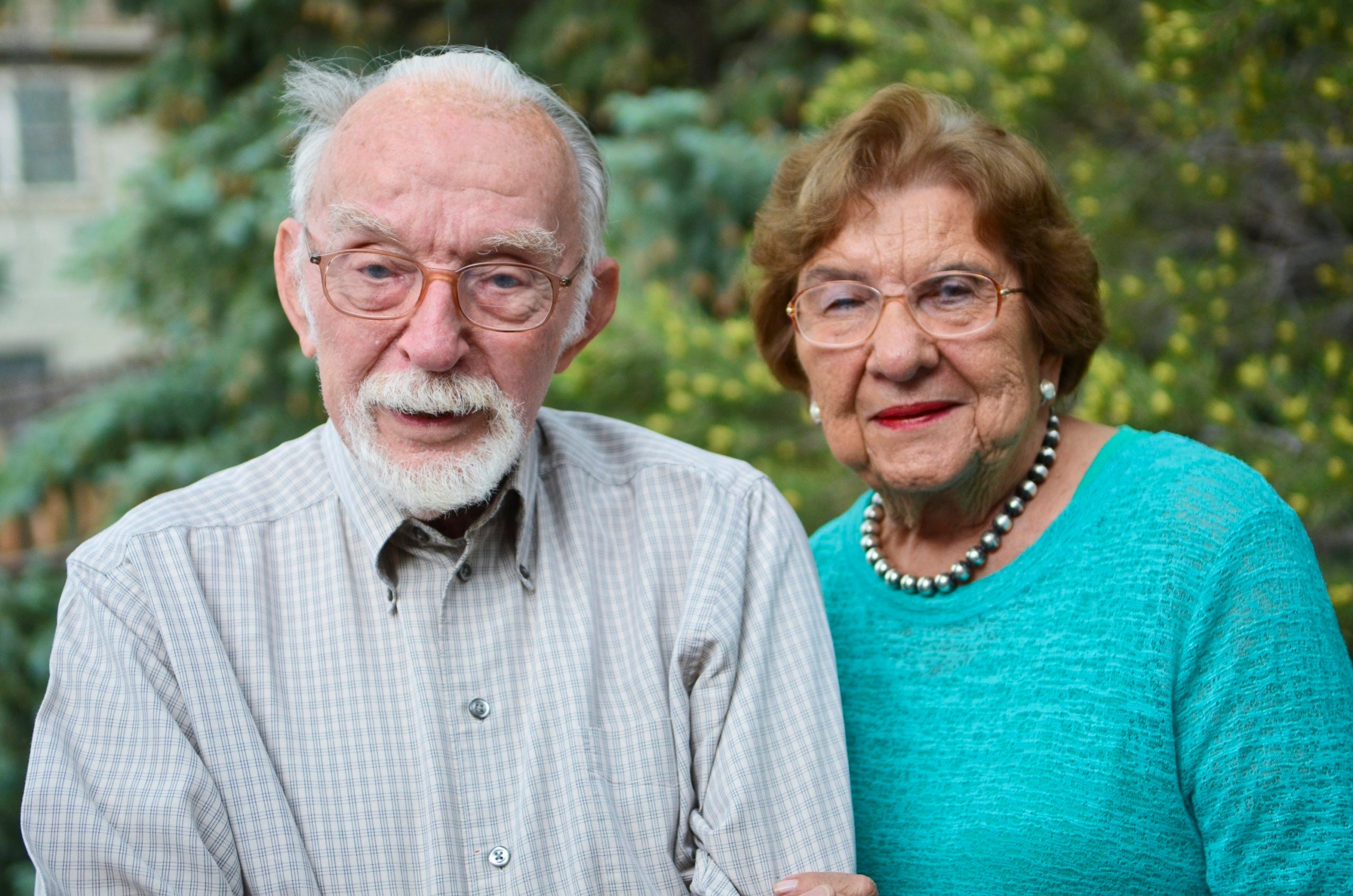 An elderly man and woman link arms and pose for the camera.