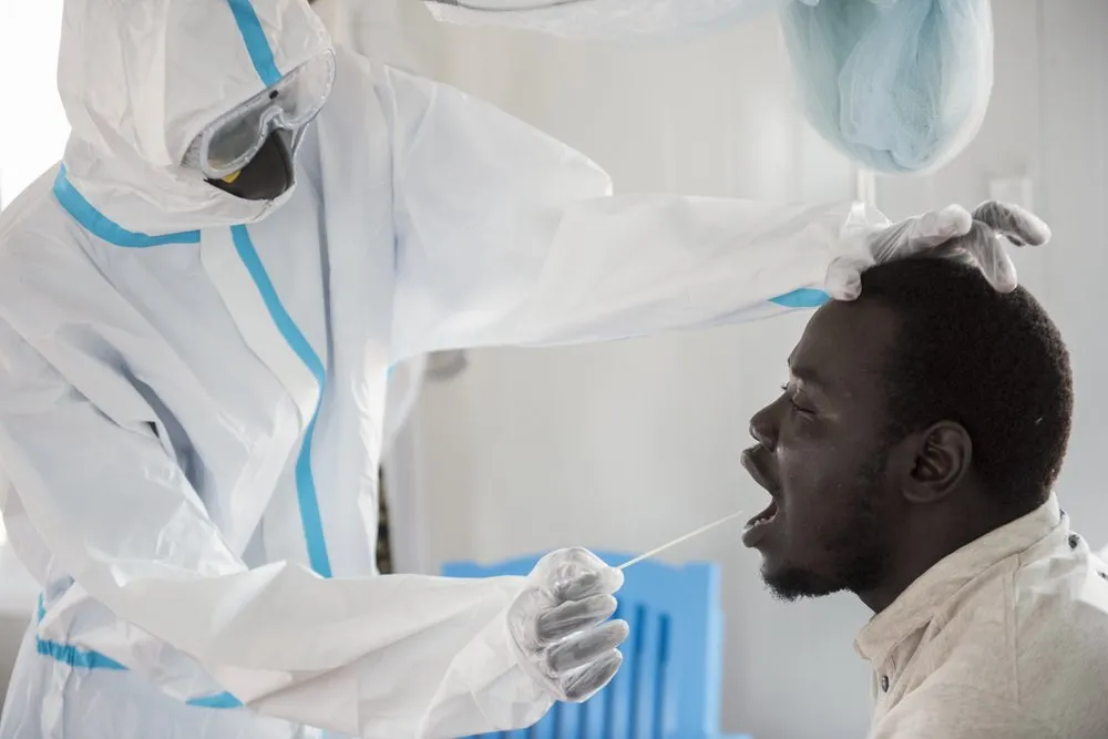 In this photo taken Sunday, June 21, 2020, an infectious disease specialist, left, takes a sample from Dr. Reagan Taban Augustino, right, now a coronavirus patient himself under quarantine, at the Dr John Garang Infectious Diseases Unit in Juba, South Sudan. The United Nations says the country's outbreak is growing rapidly, with nearly 1,900 cases, including more than 50 health workers infected, and at the only laboratory in the country that tests for the virus a team of 16 works up to 16-hour days slogging through a backlog of more than 5,000 tests. (AP Photo/Charles Atiki Lomodong)