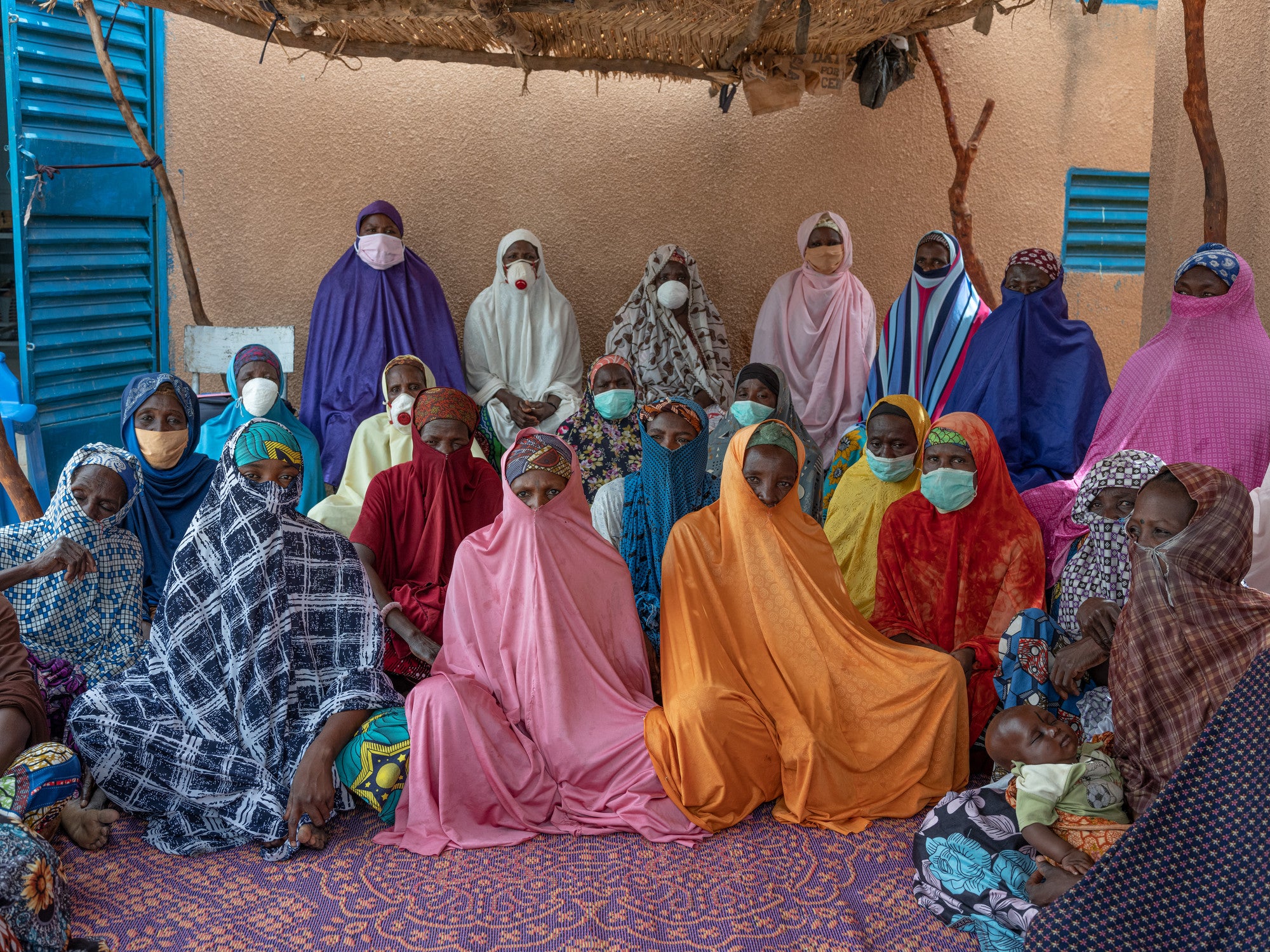 A group of women in colorful robes and face masks pose in rows facing forward.