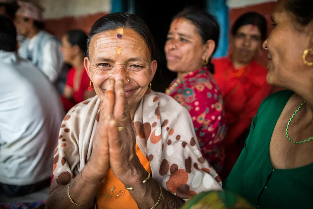 A Nepali woman smiles at the camera with her hands raised in a prayer in front of her face.