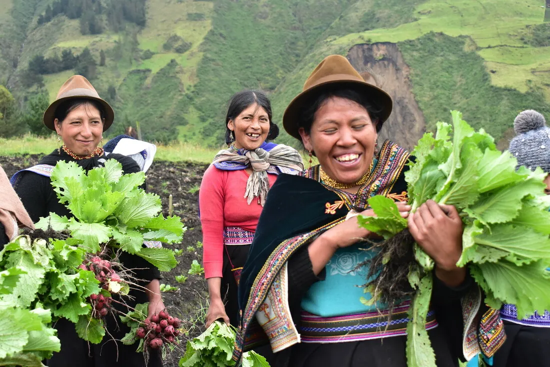 Three Guatemalan women smile while holding large heads of bright green lettuce.
