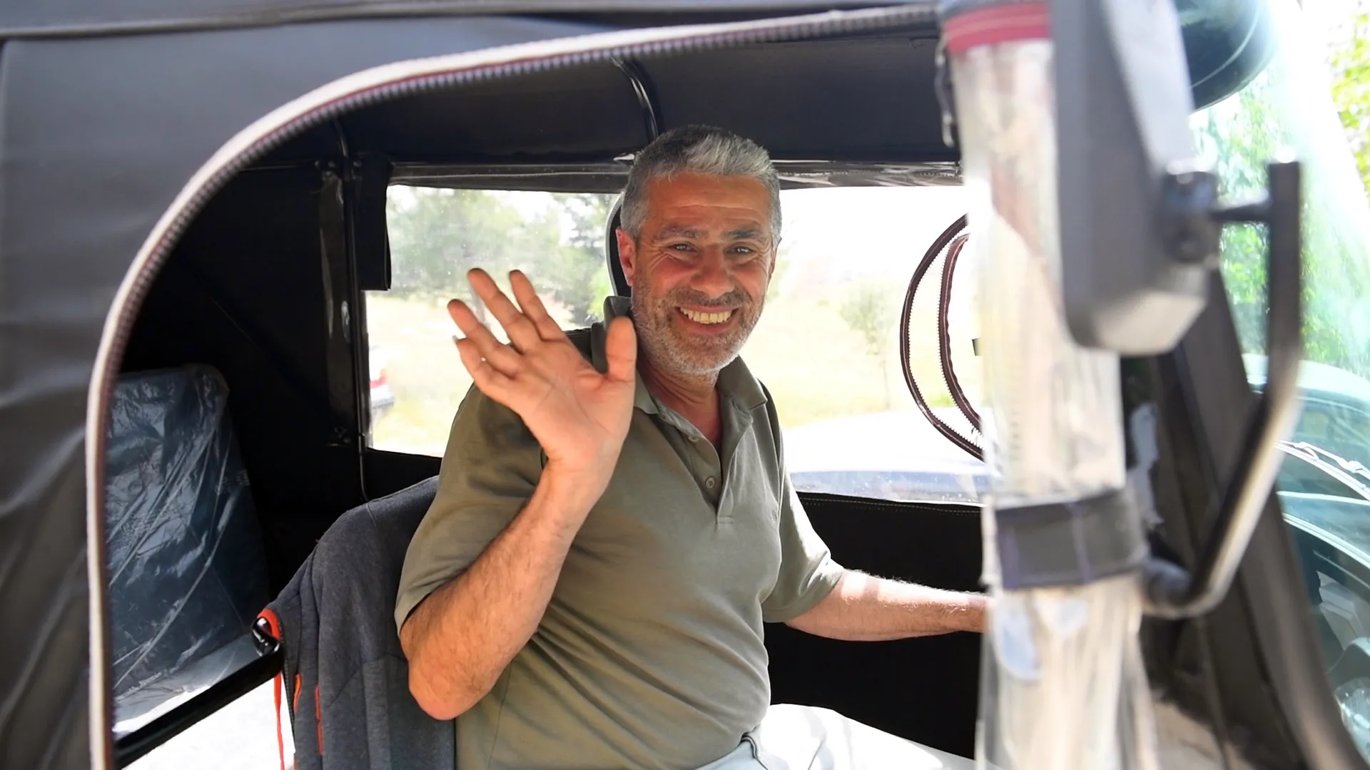 A man waving from behind the wheel of a small motorized vehicle