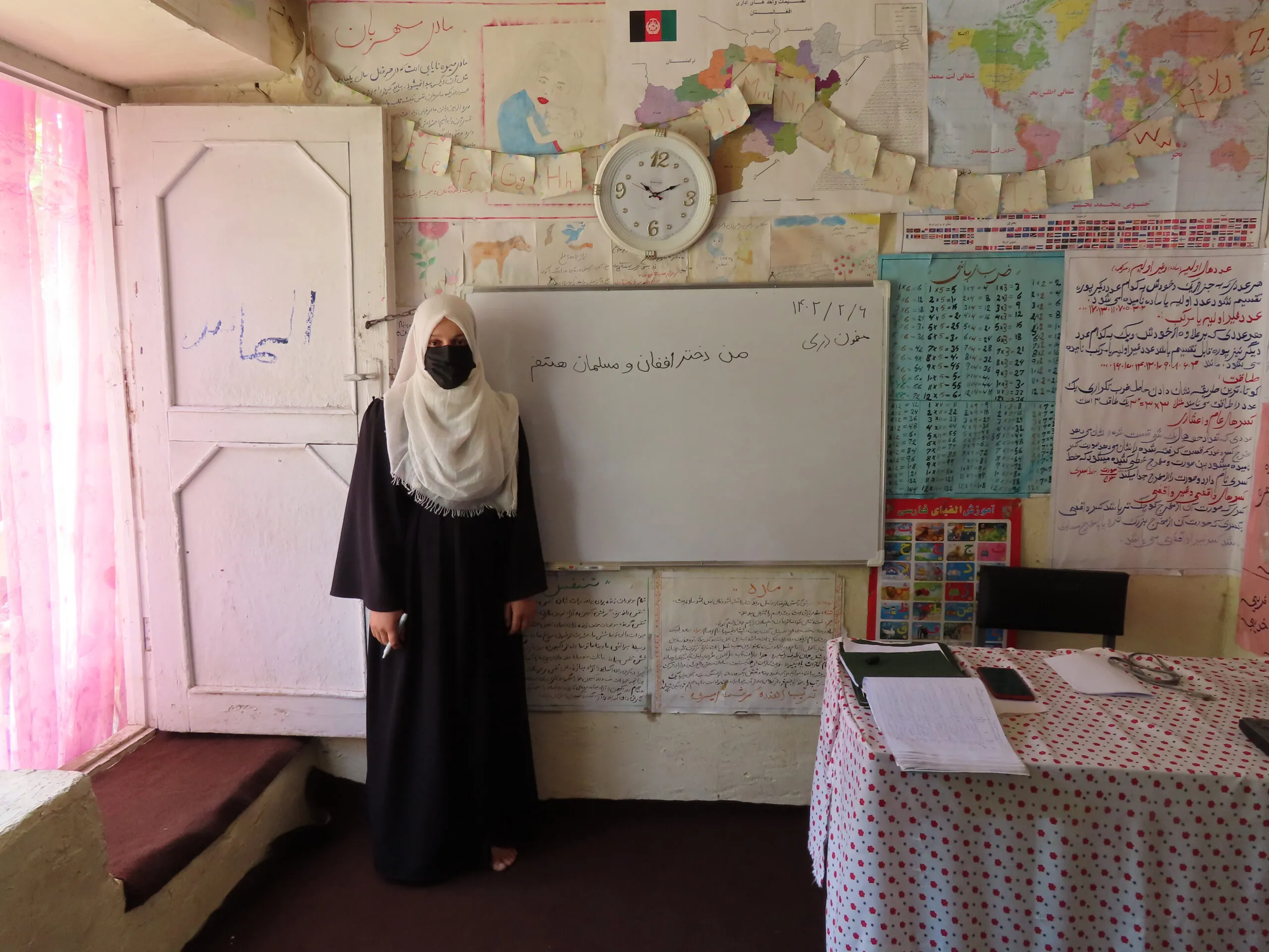 Woman in head covering and veil stands next to a whiteboard in a classroom.