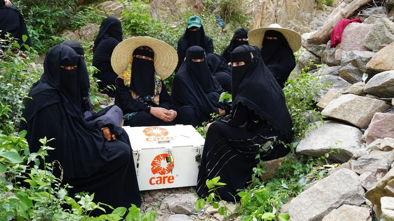 A group of women wearing black full body coverings sit around a CARE package.