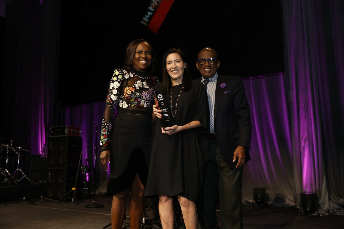 A woman holds up an award while standing in between two hosts.