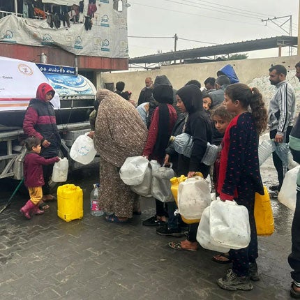 A group of people wait in line with white and yellow jerry cans.