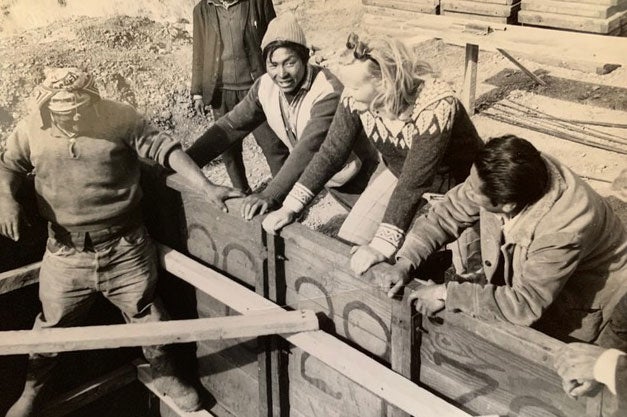 A black-and-white photo of a woman standing next to three other people to hold up a wall.