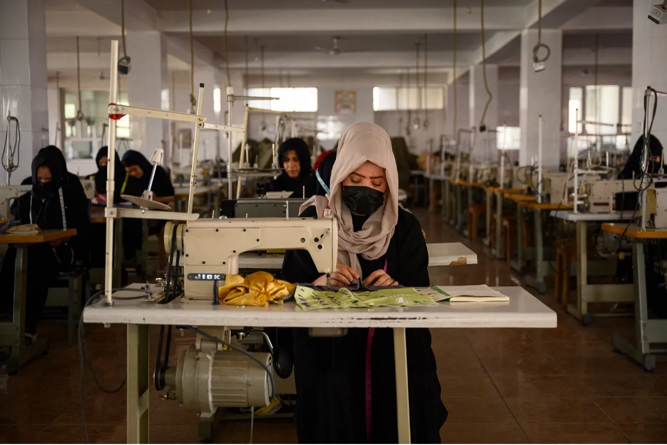 A room of women in head coverings and masks, working on sewing machines.