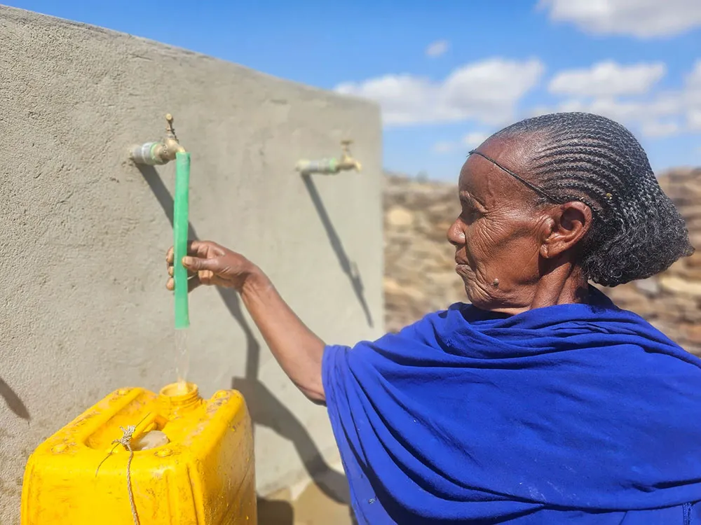 An Ethiopian woman is photographed collecting water outdoors in her yellow jerrycan from a community water point.