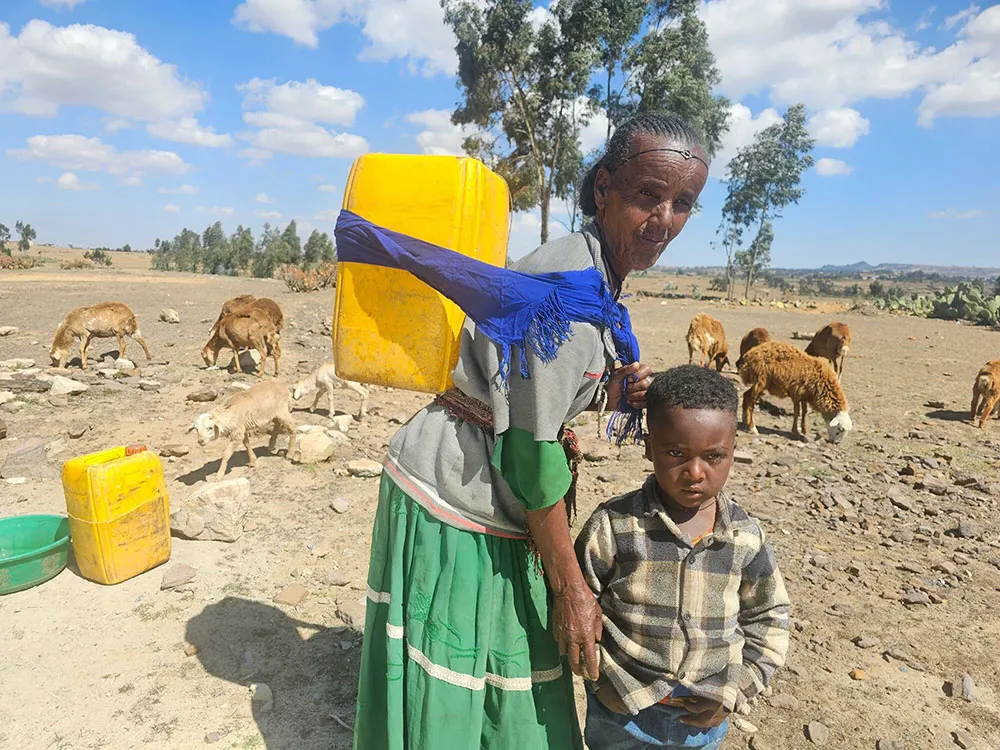 An Ethiopian woman and a little child standing with a flock of sheep in the background.