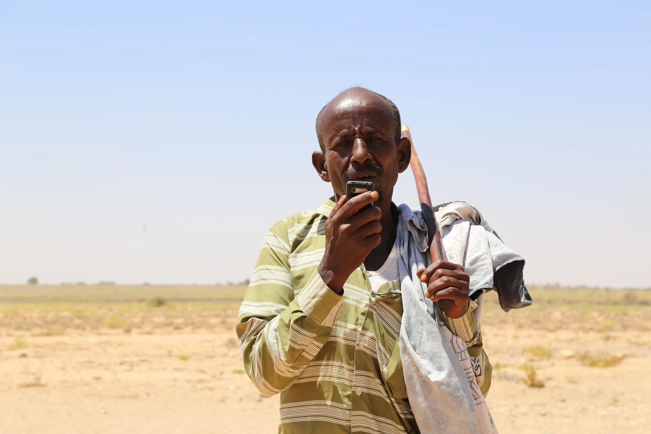 A Somalian man looking at the camera holding a mobile phone in his right hand.