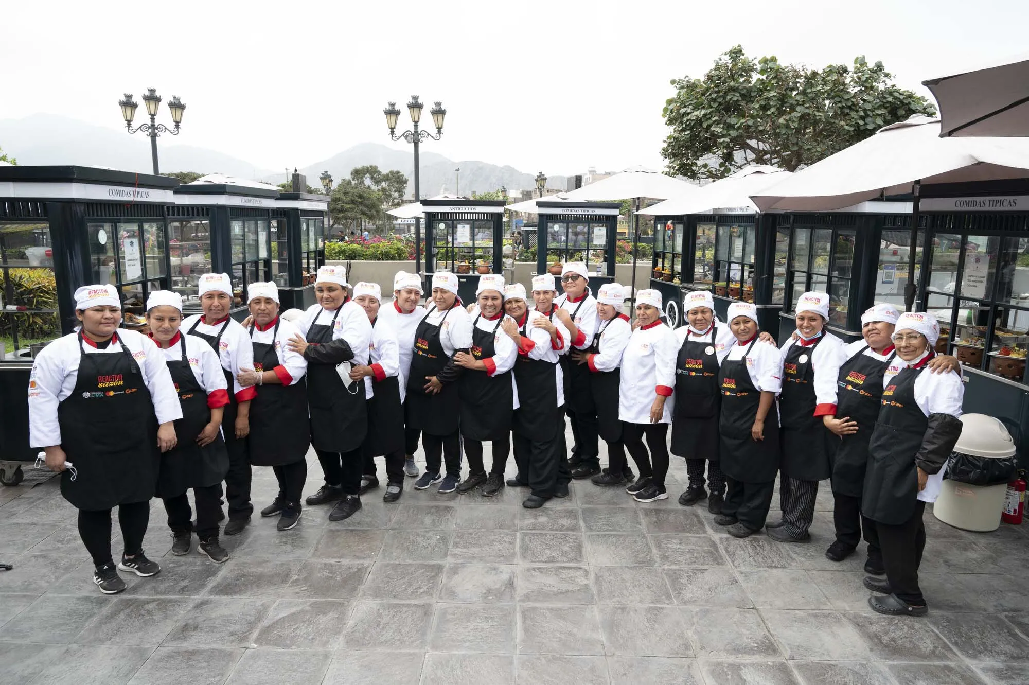 Outdoor group photo of 19 people dressed in aprons, kitchen whites and chef's hats.