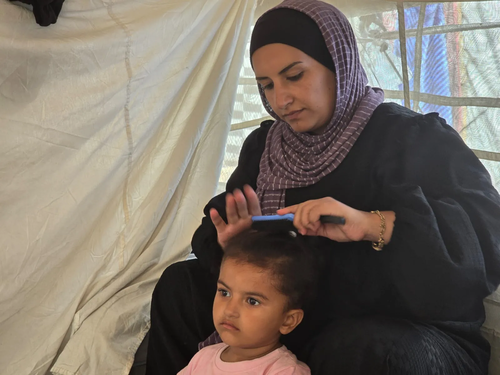 A woman in a head covering combs a child’s hair.