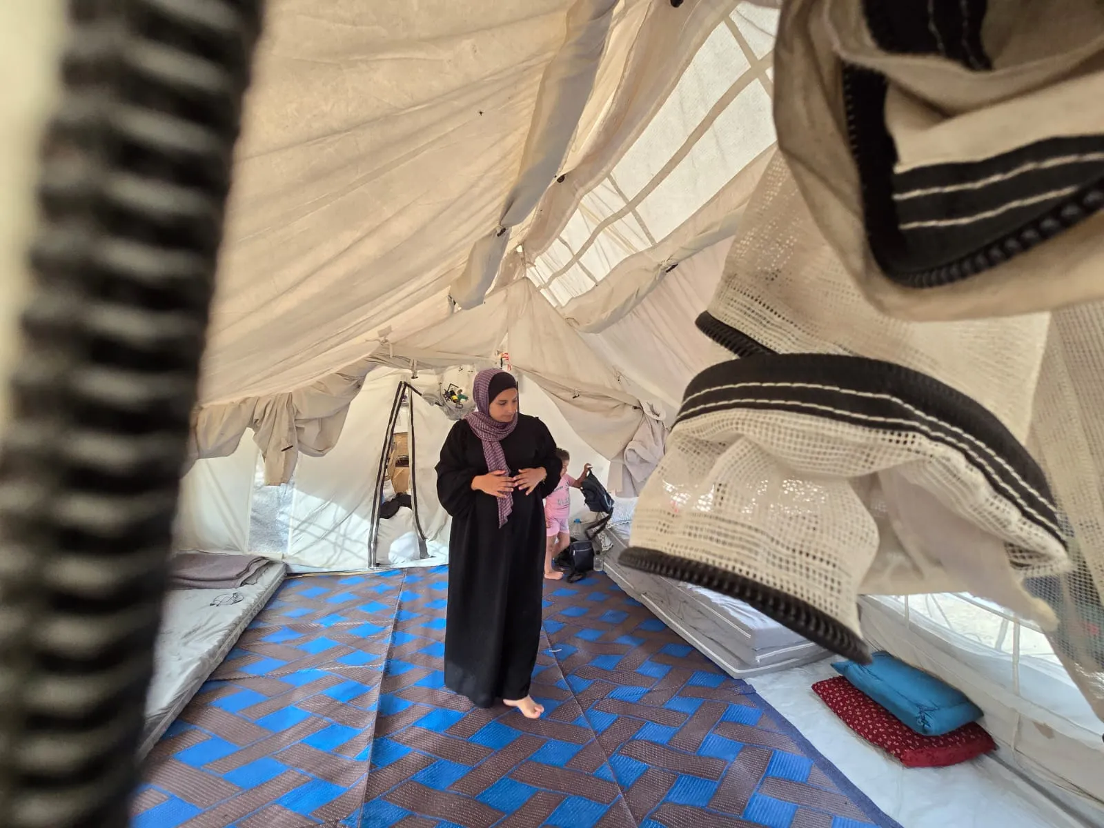 A wide-angle shot of a woman wearing black walking through a tent.