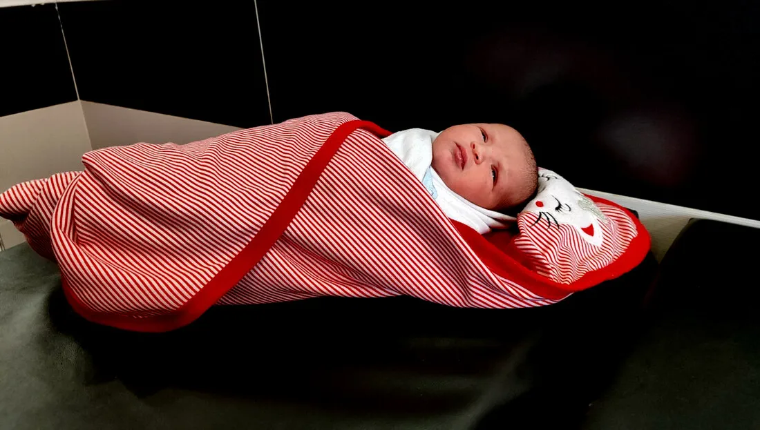 A newborn, lying down in a red striped swaddling blanket.