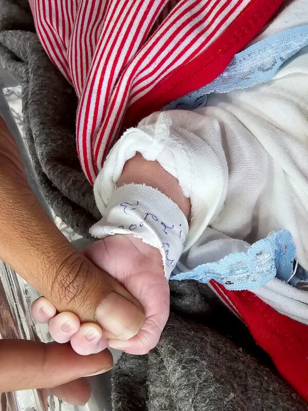 Close-up of a newborn hand gripping an adult's thumb.