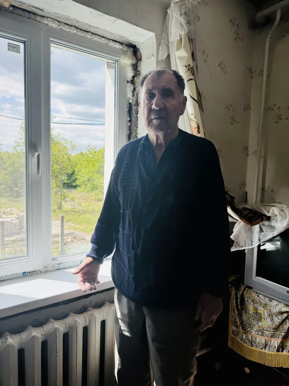 Image of an older man standing indoors, next to a window.