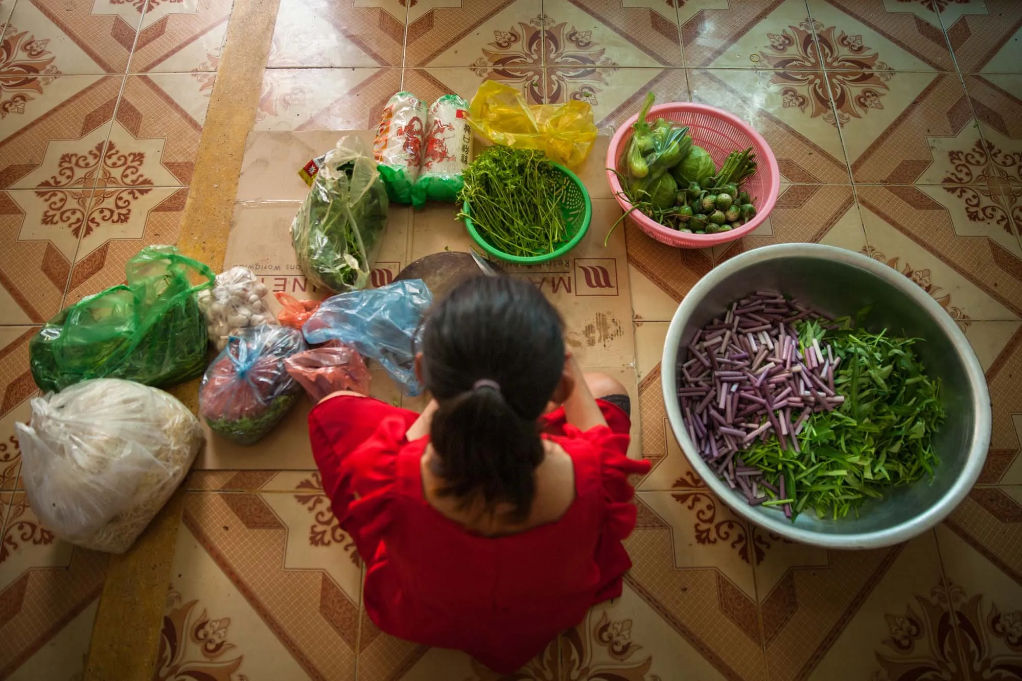 Image of a woman shot from above, sitting on the floor surrounded by bowls of greenery and vegetables