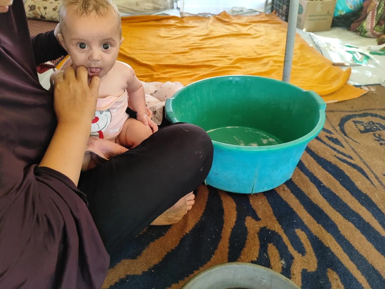 A displaced Palestinian mother is seen washing her little child inside a makeshift tent.