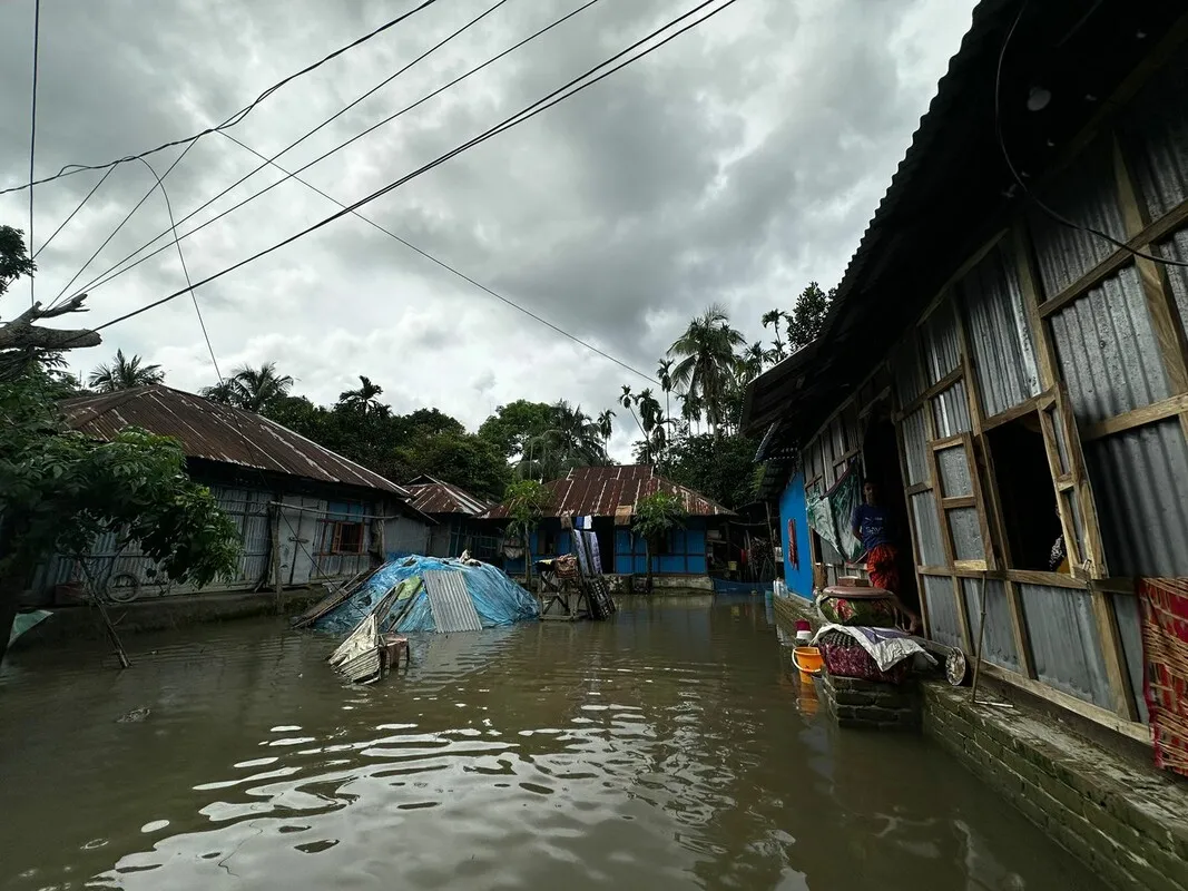 A flooded courtyard surrounded by tin-roofed houses. A resident looks out from one of the houses, surveying the damage