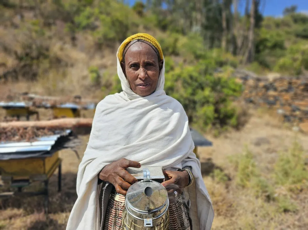 Ethiopian woman, a beekeeper, holding a steel jar-like thing, presumably used to create smoke in the hive.