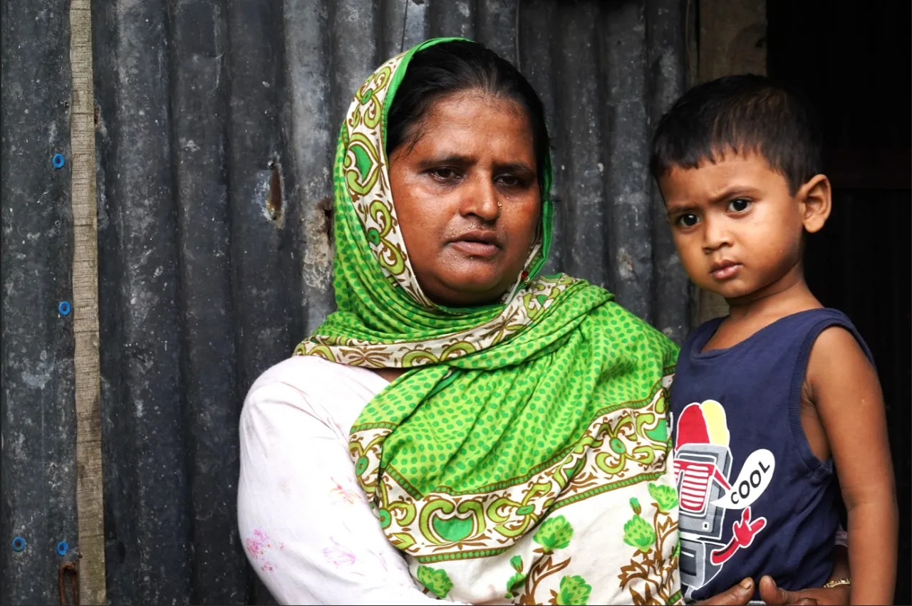 A close-up of a worried mother holding her child on her lap, looking away from the camera. She appears stressed and overwhelmed