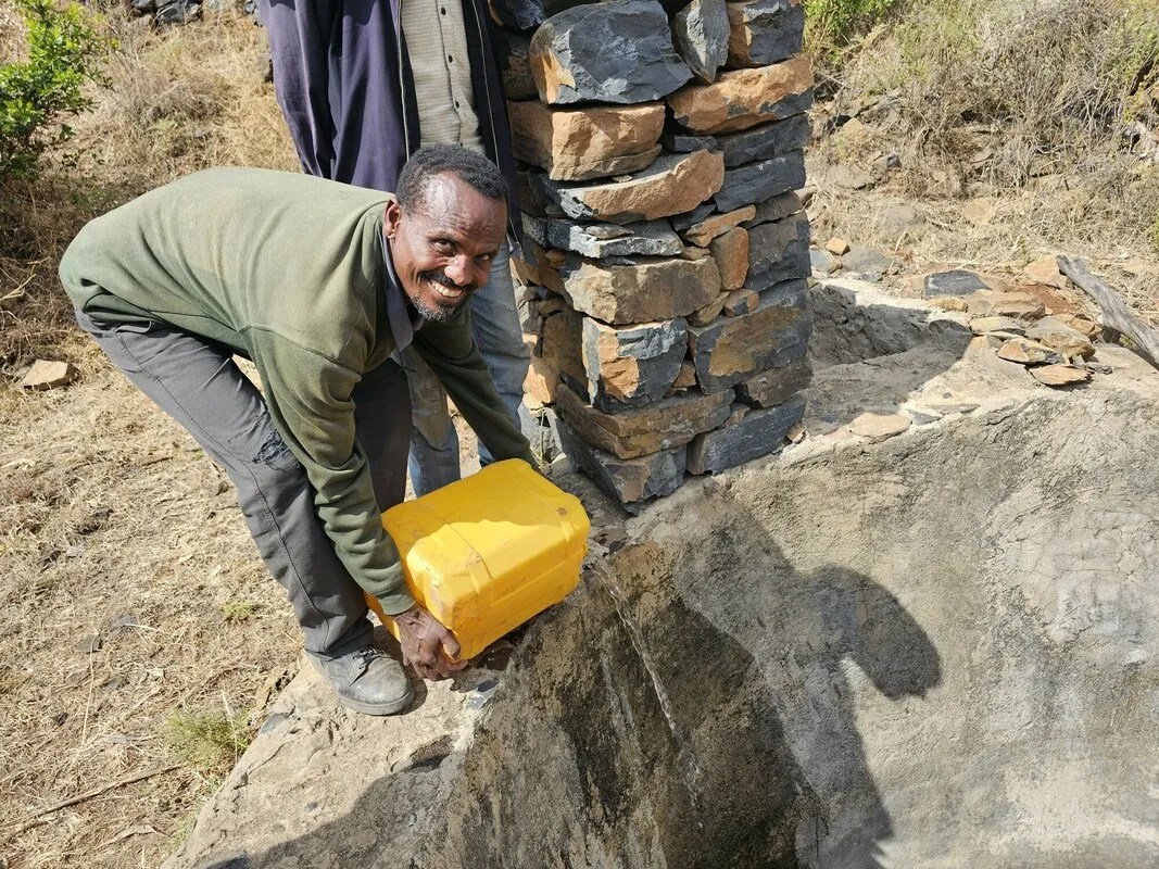 Gerbregergis from Ethiopia smiling while pouring water from a yellow jerry can into a reservoir.