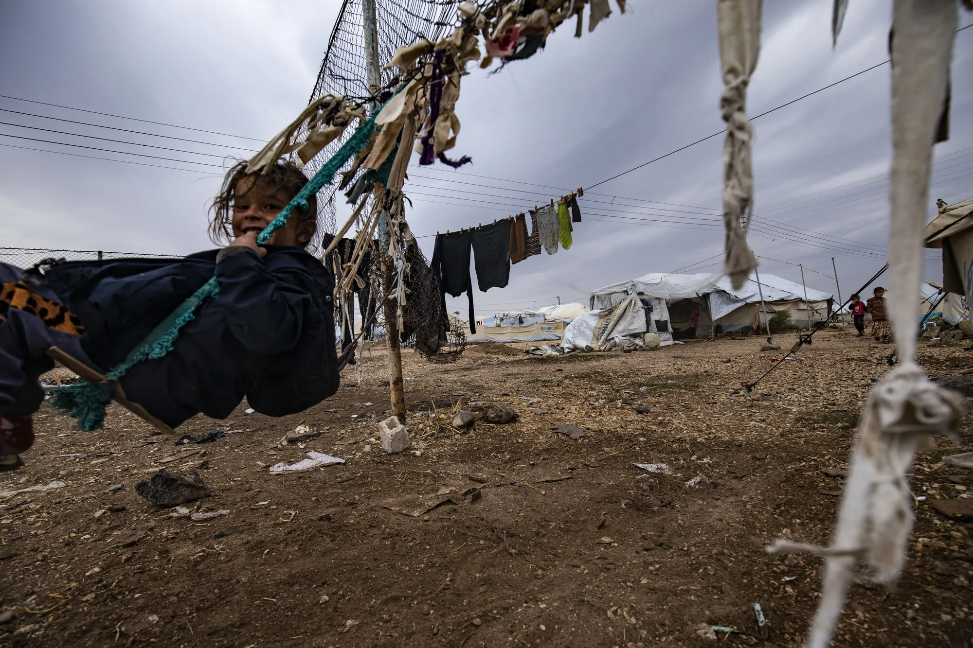 A Syrian child smiles at the camera while swinging in a makeshift camp for internally displaced people.