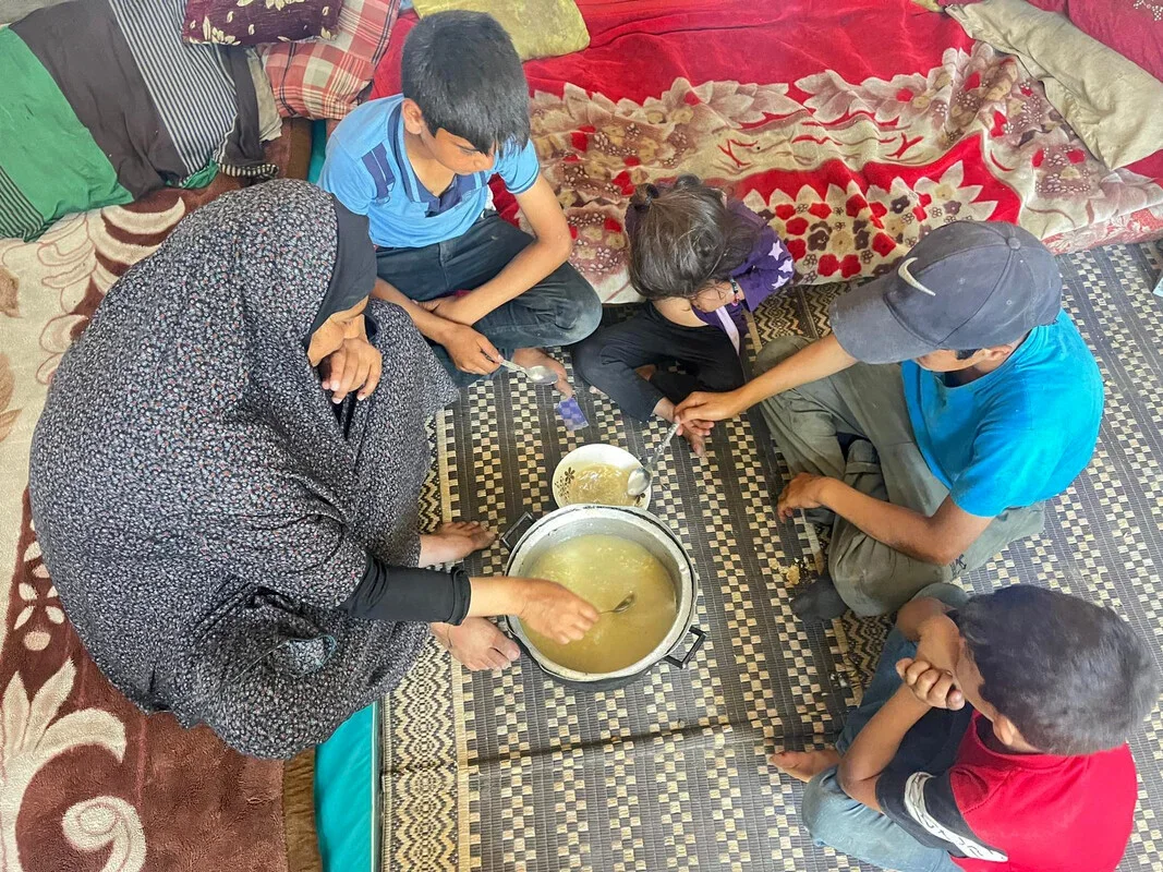 A family of five, including three boys and one girl, enjoys a meal together in a makeshift tent.