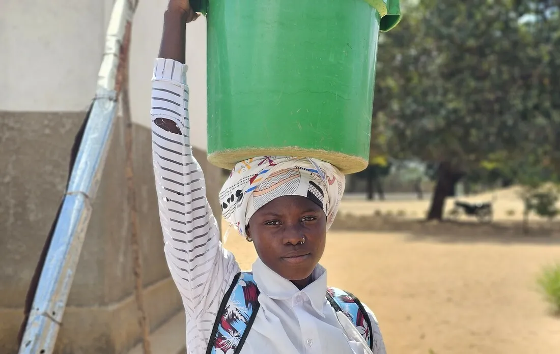 Farsana, a girl from northern Mozambique, carrying a bucket of water on her head.