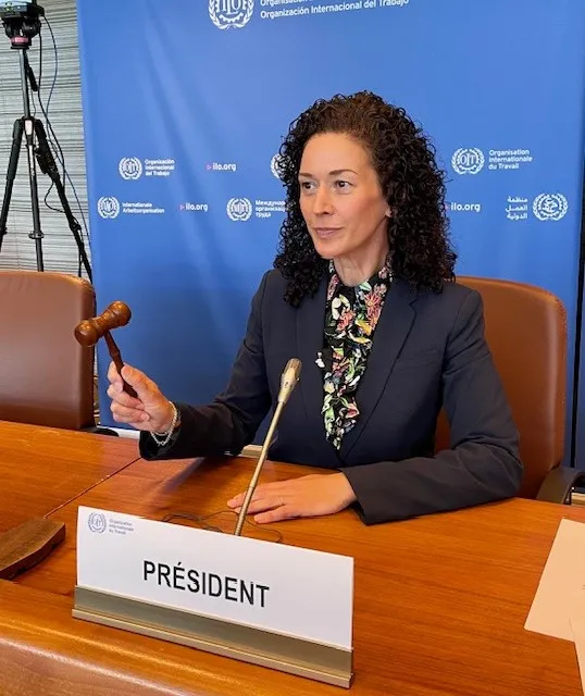 A woman sitting behind a desk raises a gavel.