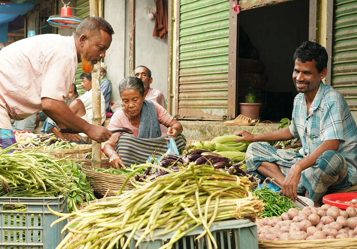 A group of people sit and look through veggies in a market.