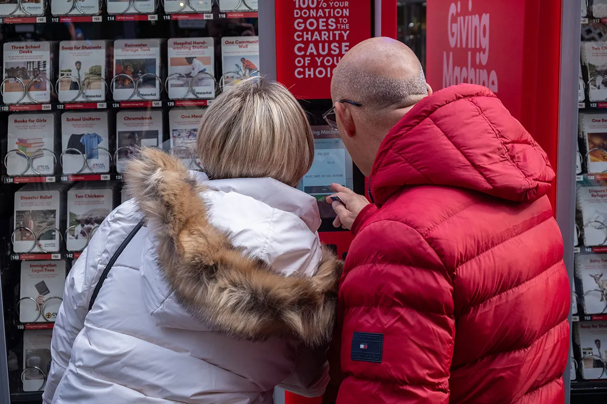 A man and woman look through options at a red Giving Machine.