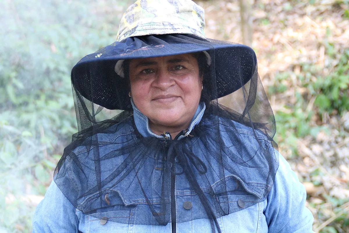 A woman wears a mesh beekeeping hat.