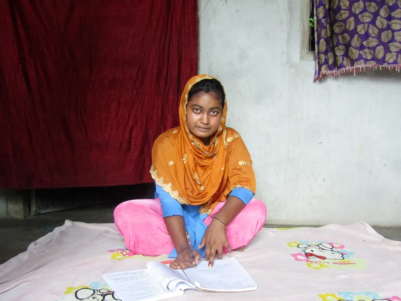 A school girl sits on the floor and reads an open workbook.