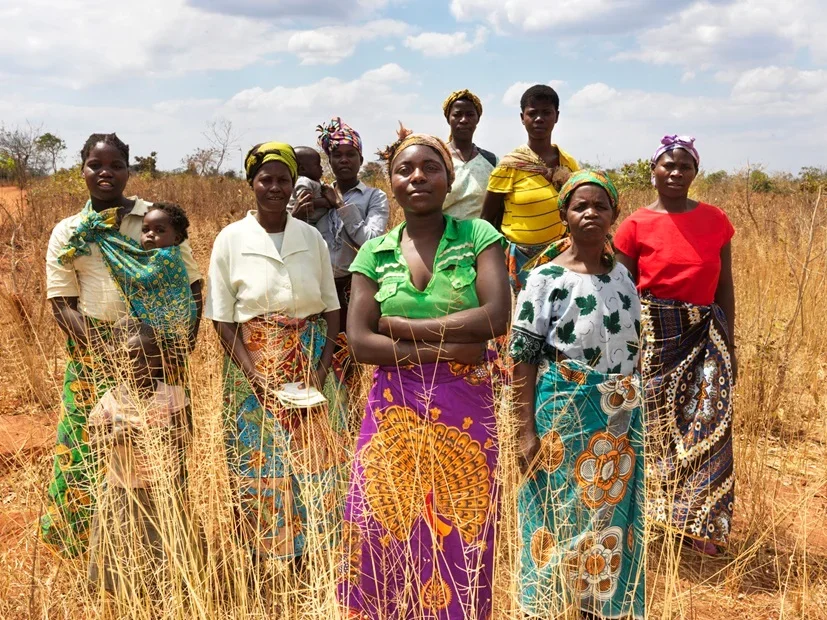 A group of women, two carrying small children, stand together in a field.