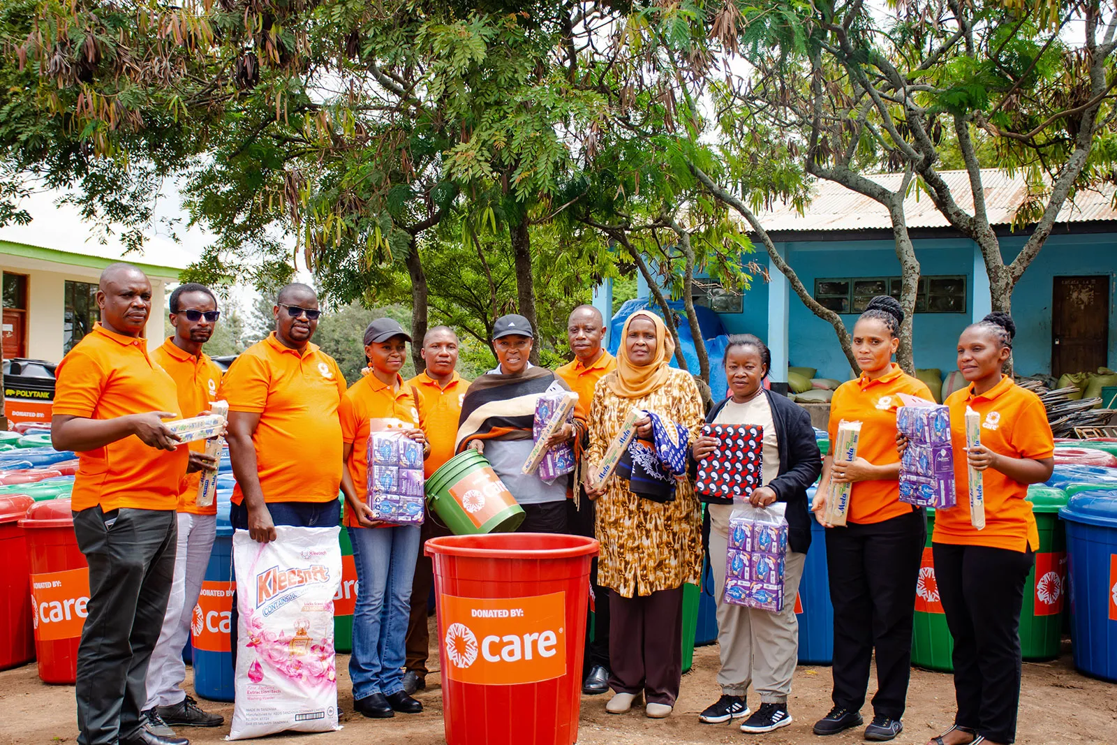 A group of people wearing orange CARE shirts stand together holding supplies.