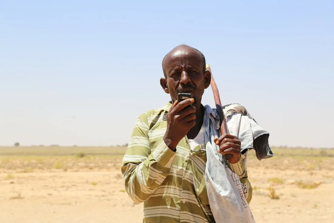 A man standing in a field talks through a walkie talkie.