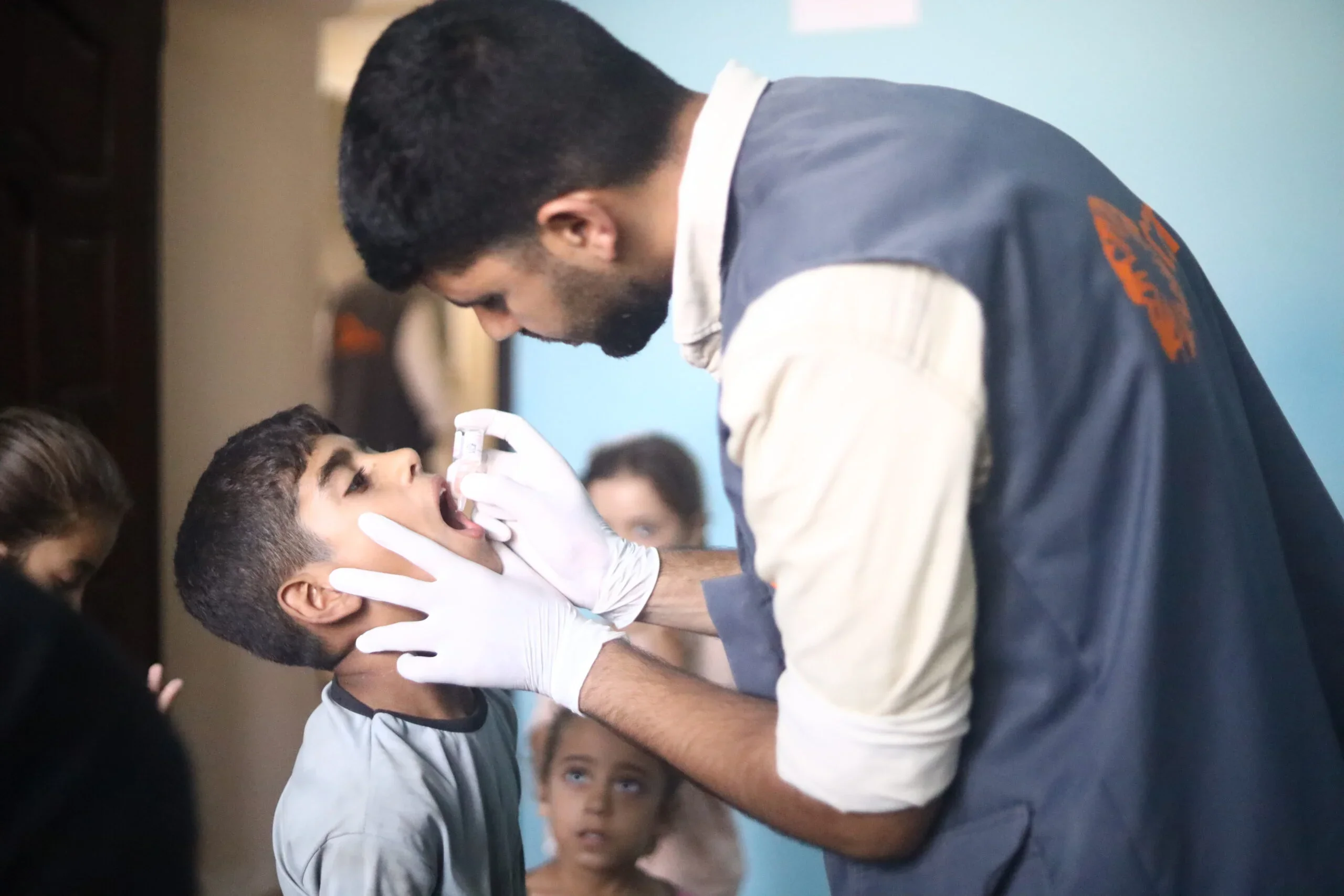 A man wearing a CARE vest and medical gloves peers into a young boy's mouth with a light.