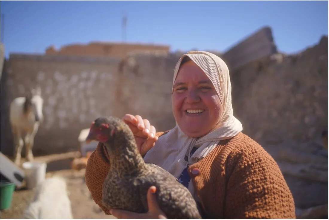 A woman smiles while holding a chicken.