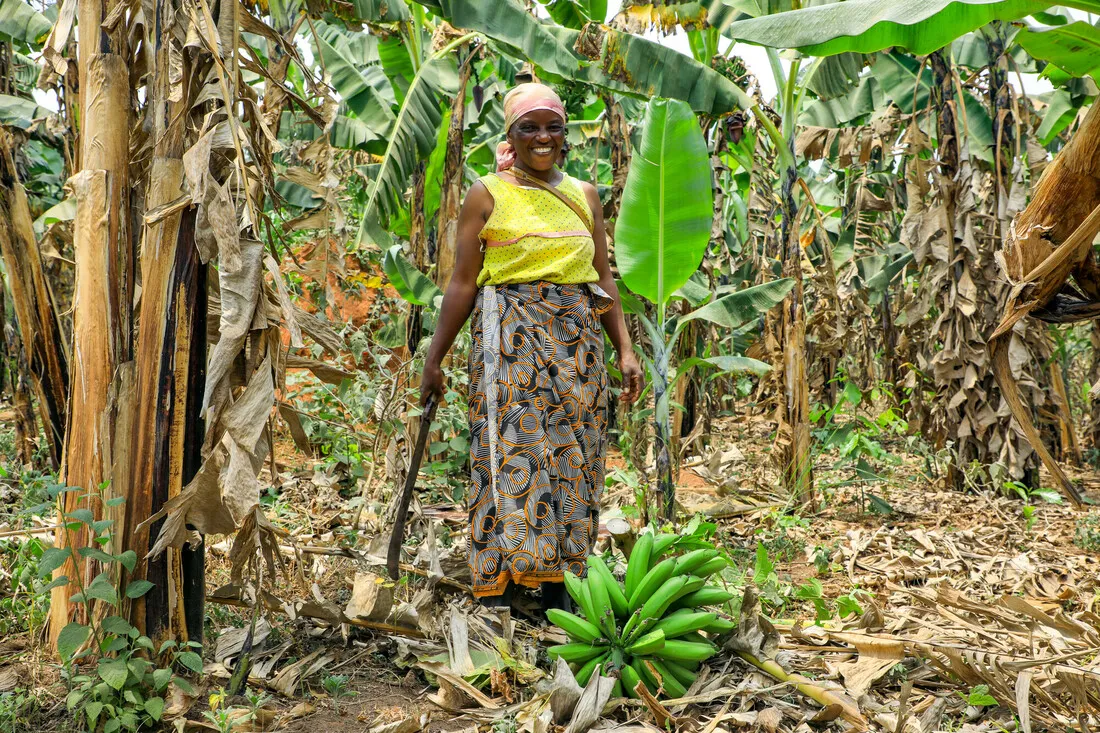 A woman holds a machete while standing in a forest.