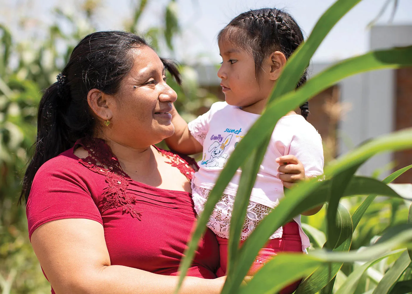 A woman holds up a small girl while standing in a field of bright green crops.