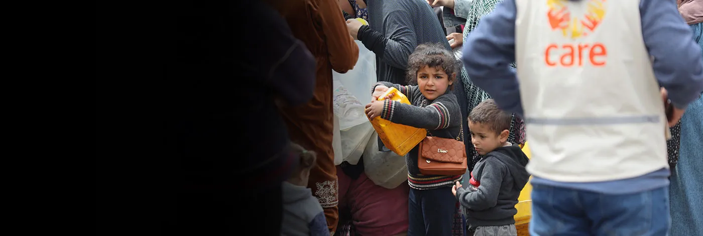 Two kids hold a jug of water next to a man wearing a CARE vest.