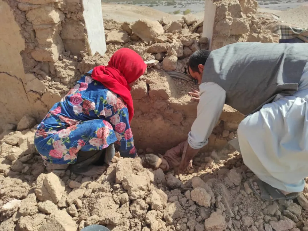 An Afghan man and a woman work together to lift a young boy trapped beneath the rubble, after an earthquake.