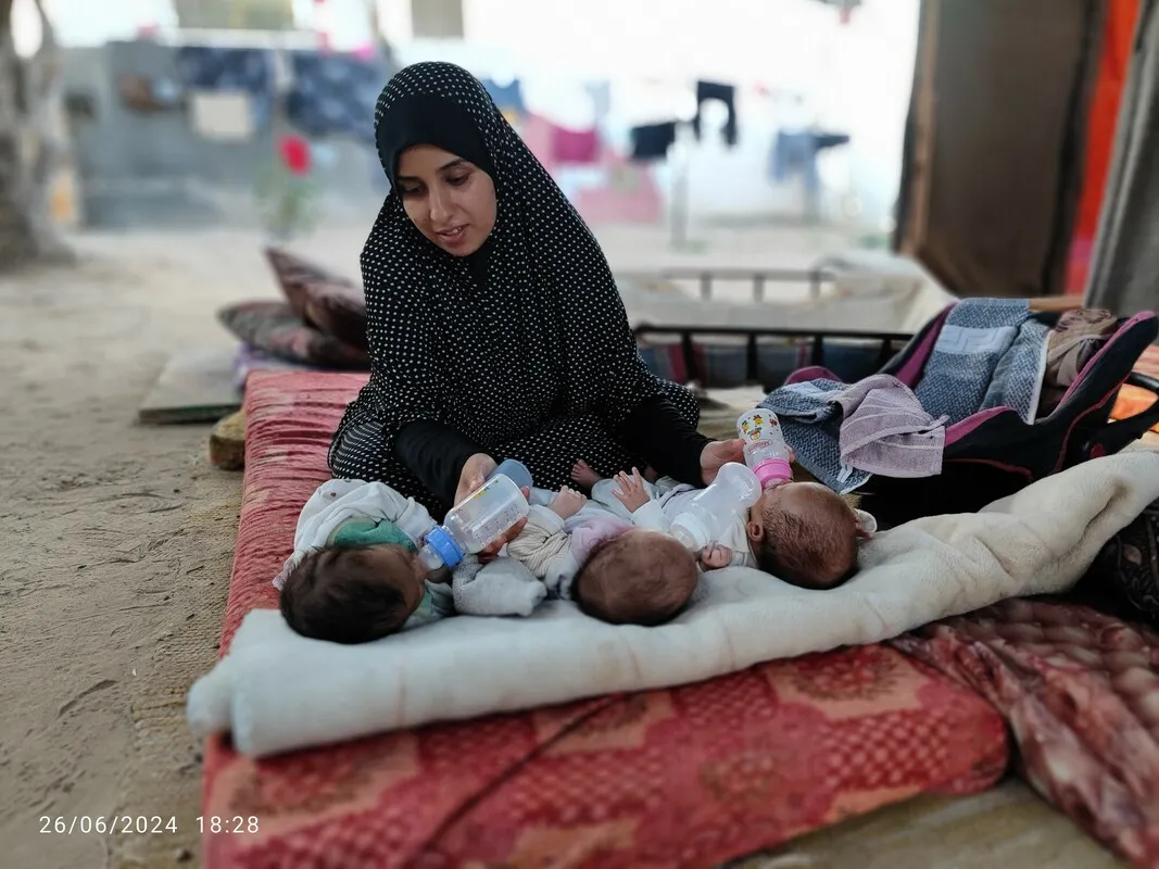 A mother in Gaza feeds two of her triplet babies, holding two bottles in her hands.