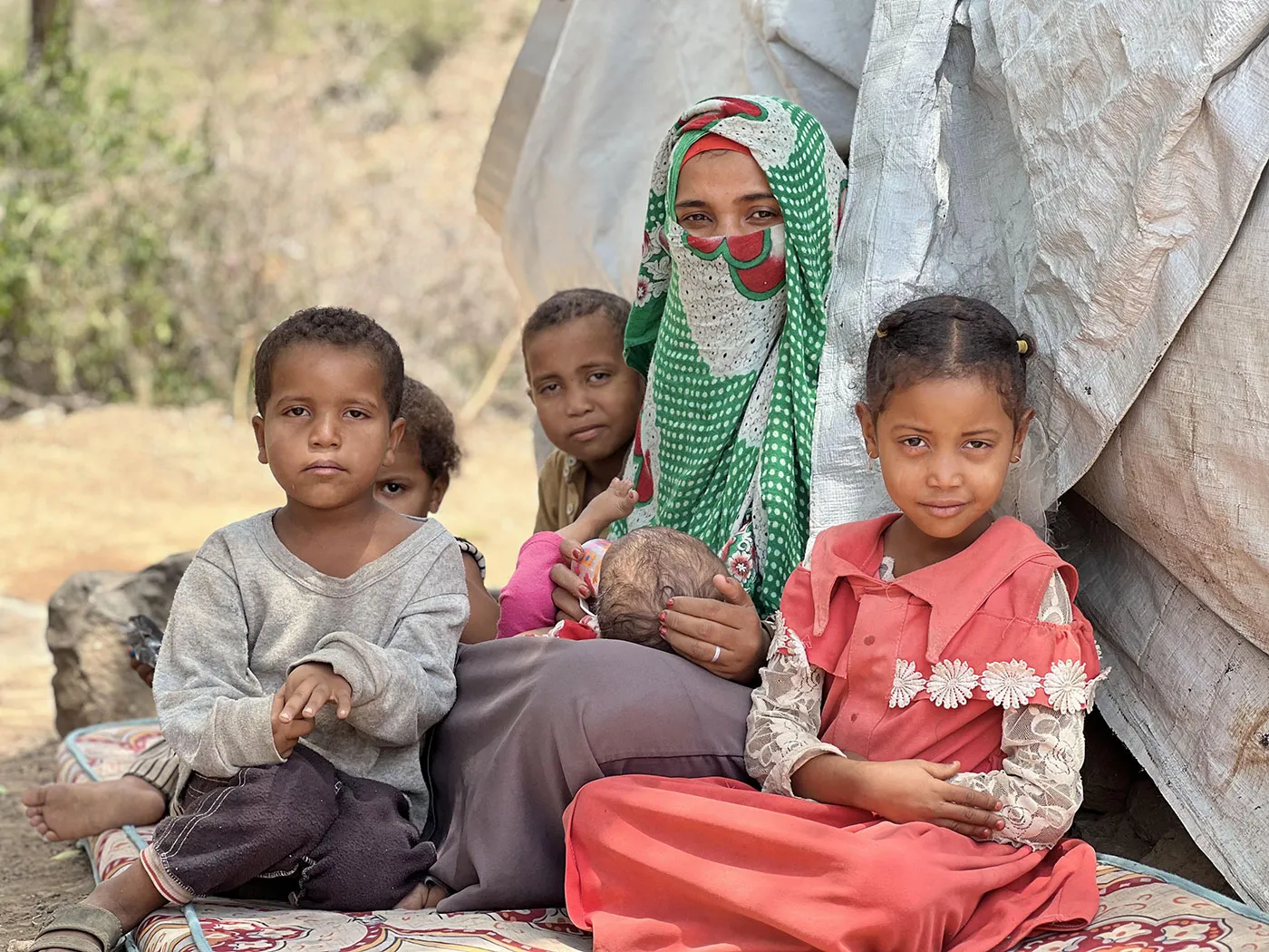 A Yemeni woman sits outside a tent with four children.