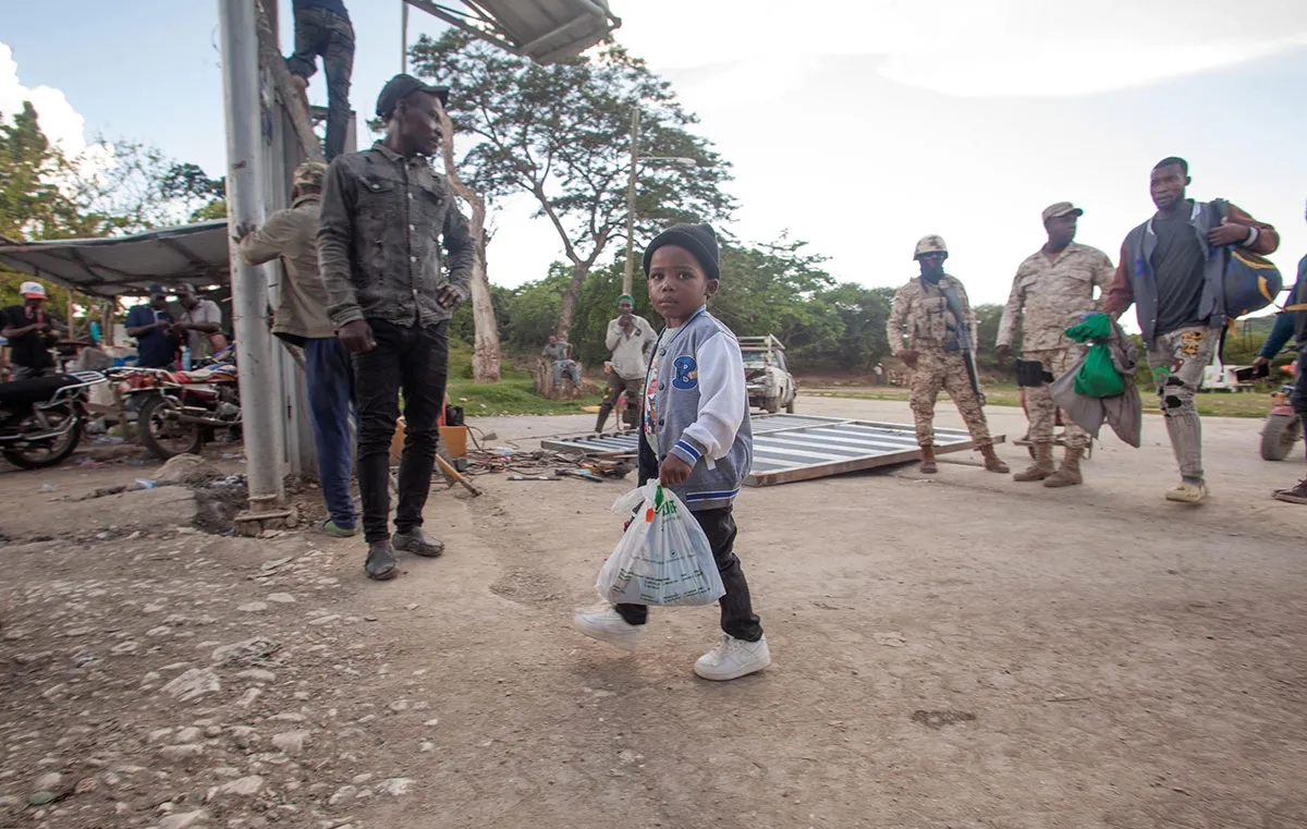 A young boy carries a plastic bag full of clothes.