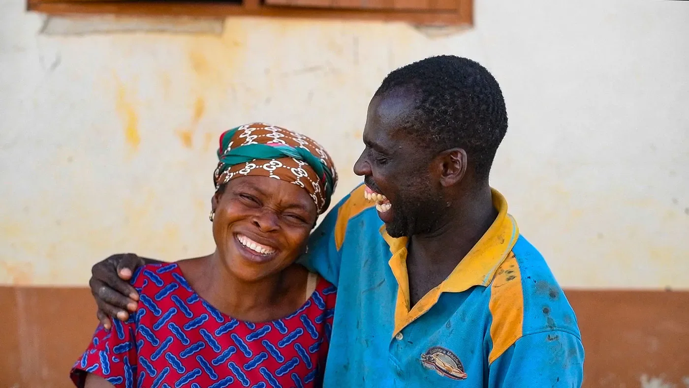 A Ghanian man and woman laugh and hug each other.