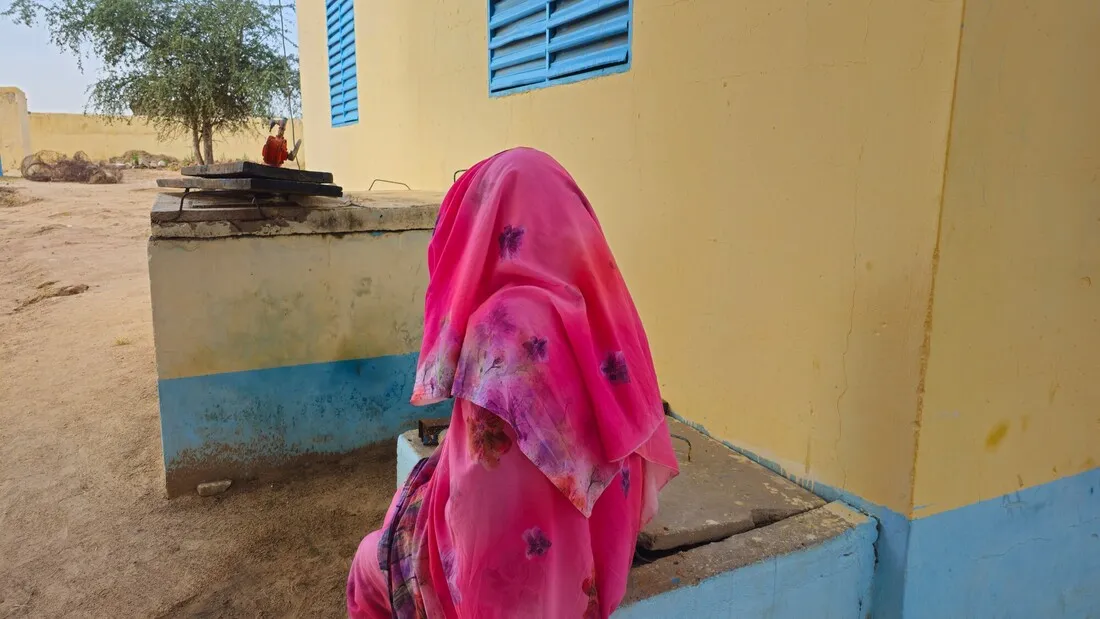 A woman from Chad, viewed from behind, next to a building.