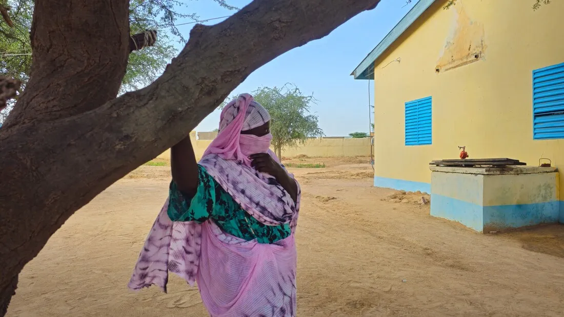 A woman from Chad, standing outdoors with a house in the background.